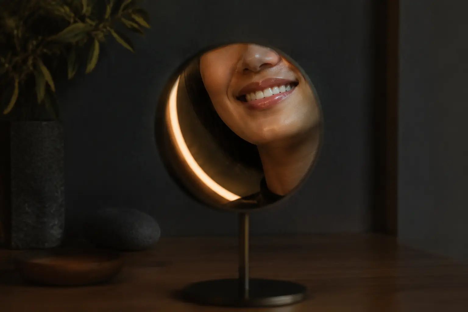 Natural fictional adult smile reflected in a small studio mirror beside a warm curved ring of light